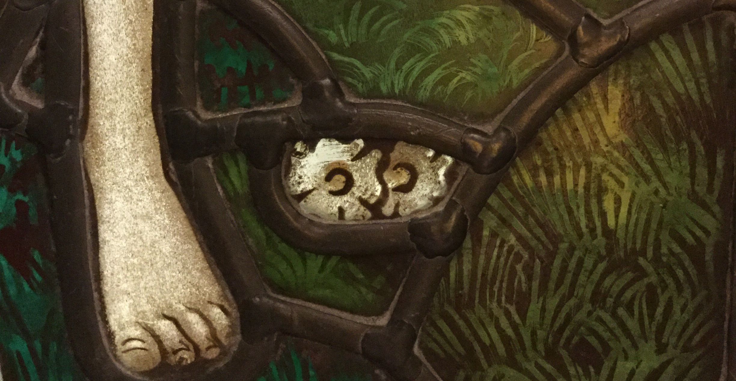 Detail of stained glass window, showing a foot and two white flowers, also visible as a cat’s face