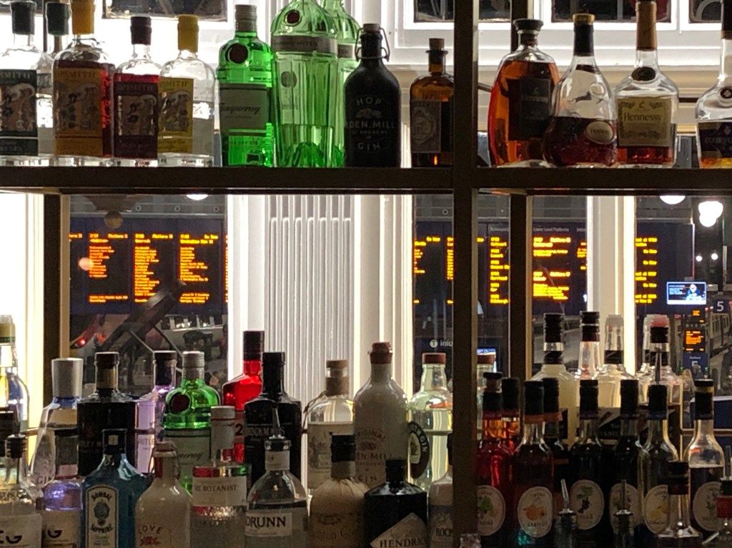 View through an assortment of bottles of spirits to the departure boards at Glasgow Central