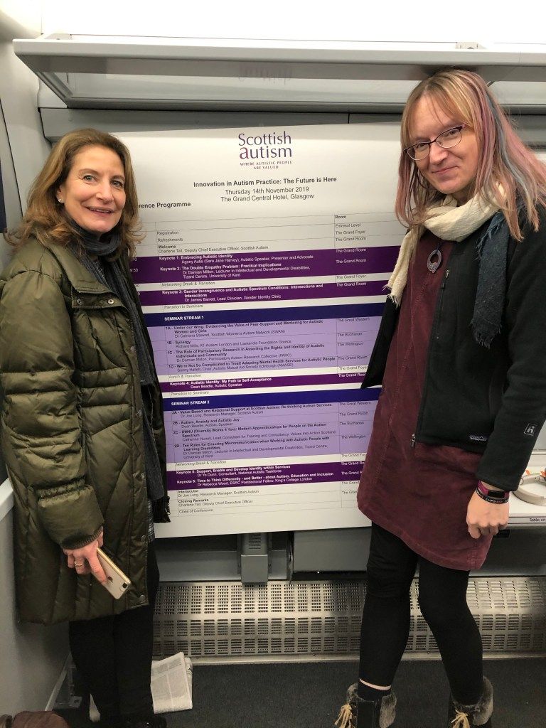 Fiona and Anna on a ScotRail train with a large (A0?) poster board with information about conference sessions