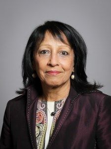 Kishwer Falkner, a middle-aged Pakistani woman with shoulder-length black hair, wearing large pearl-like earrings and a deep burgundy satin jacket over a patterned top.
